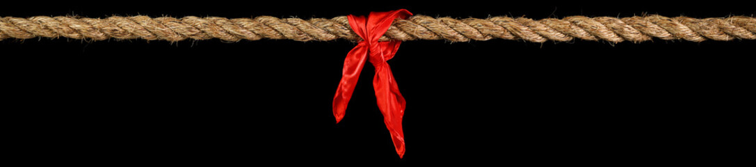 Long tug of war rope pulled tight, with red ribbon tie. Concept of conflict, competition, or rivalry.  Isolated on black.