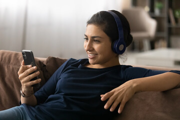 Happy millennial Indian woman in headphones have webcam digital virtual conference on cellphone. Smiling young ethnic female in earphones talk speak on video call on smartphone. Technology concept.