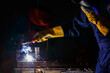 © Bangkok Click Studio - a factory worker wearing a green mechanic coveralls and safety helmet welding metalwork at night time in a factory while his colleague looking at a spark from welding