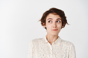 Wall Mural - Cute young woman with shirt haircut, looking tempted at upper left corner empty space, thinking about something, standing pensive on white background