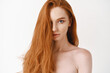 Close-up of beautiful young woman with long healthy red hair looking at camera. Pale female redhead model gazing sensual, white background