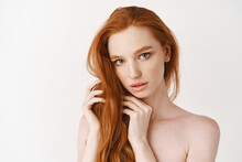 Beauty. Young Woman With Natural Shiny Red Hair And Perfect Pale Skin Looking At Camera, Sensual Gaze, Standing Naked Over White Background