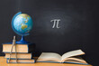The Greek letter Pi, the ratio of the circumference to its diameter, is drawn in chalk on a black school board with books, a globe and a compass in honor of the international number Pi for March 14