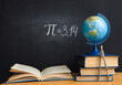 The Greek letter Pi, the ratio of the circumference to its diameter, is drawn in chalk on a black school board with books, a globe and a compass in honor of the international number Pi for March 14