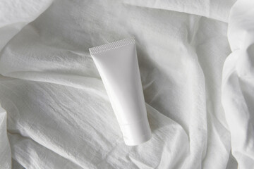 Top view mockup blank white label packaging organic facial gentle skincare white tube product with minimal soft crumpled white fabric cloth as a background