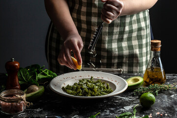 Woman hands cooking Penne pasta and adding cheese parmesan in dish. sprinkling with cheese on green pasta with spinach and green pesto