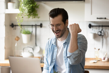 Wall Mural - Overjoyed young Caucasian man look at computer screen feel euphoric read good news in email letter. Happy excited millennial male celebrate online lottery win on laptop. Luck, success concept.