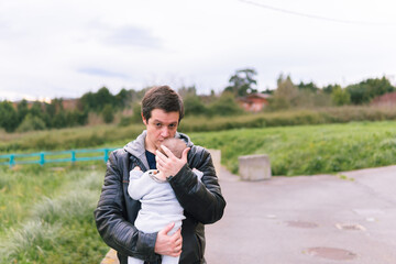 Middle-aged young attractive man holding his six-month-old baby in spring in leather jacket and jeans. spring summer fashion parenting concept.