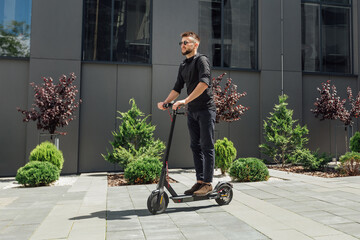 Wall Mural - Young man riding electric scooter in urban background