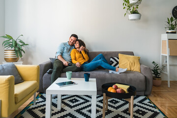 embraced couple relaxing together on their sofa at living room in home. happy couple having romantic