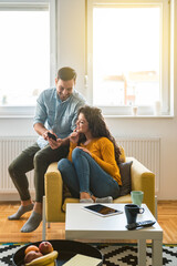 Wall Mural - Smiling couple talking and looking in mobile phone. Loving couple laughing and watching something on smartphone together at home