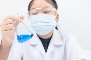 Wall Mural - a little scientist is looking at blue liquid chemical in beaker isolated