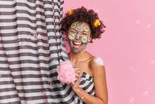 People Hygiene And Cleanliness Concept. Overjoyed Ethnic Woman Has Fun In Douche Takes Shower Holds Sponge Poses Naked Behind Curtain Undergoes Beauty Treatments Applies Nourishing Clay Mask