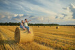 © MNStudio - Adorable young sisters having fun in a wheat field on a summer day. Children playing at hay bale field during harvest time. Kids enjoying warm sunset outdoors.