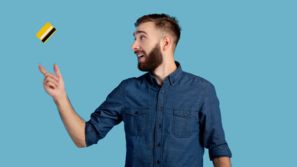 Millennial hipster guy catching credit card on blue studio background, panorama. Contactless payment solutions concept