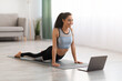 © Prostock-studio - Athletic young woman doing yoga in living room, using laptop