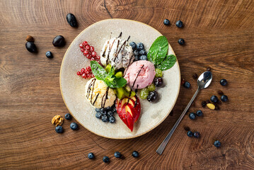 Wall Mural - 
Ice cream dessert. Three multi-colored balls of ice cream, decorated with fruits, berries and mint, on a large plate 