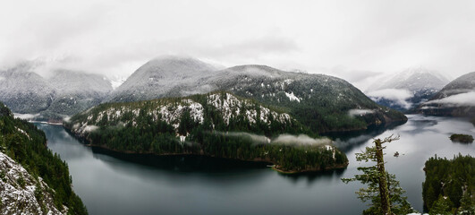 Wall Mural - A panorama of a mountain lake in winter surrounded by snow covered pine trees.