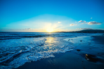 Wall Mural - Sun shining over Alghero sandy shore at sunset