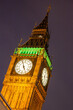 Big Ben clock face illuminated at night with dark skies behind with orange and green lights on the clock of Elizabeth Tower next to the Houses of Parliament in Westminster,, London, England