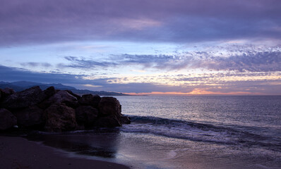 Picturesque scene of the purple toned sunset above sea waters seen through the rocky shore