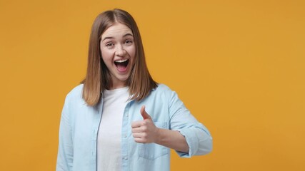 Wall Mural - Back rear view of cheerful blonde young woman 20s years old in blue shirt posing isolated on yellow background in studio. People lifestyle concept. Turns around camera showing thumbs up like gesture