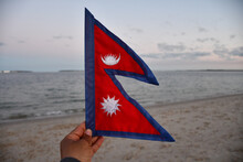Selective Focus Of A Hand Holding The Flag Of Nepal On Blurred Sea Background