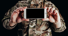 Photo Of Soldier In Camouflaged Uniform Holding Smartphone On Black Background.