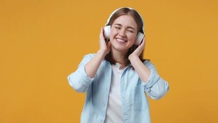 Wall Mural - Cheerful funny blonde young woman 20s years old in casual blue shirt posing isolated on yellow background studio. People lifestyle concept. Listening music with headphones dancing waving rising hands