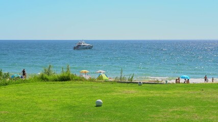 Wall Mural - Sight of a grassy golf field, a clear blue ocean with a yacht in the distance and some people on the beach. Vale do Lobo, Portugal.