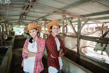 close up of a couple farmer wearing a hat standing back to back smiling looking at the camera in the cattle breeding stable