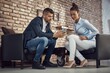 © nyul - Businessman and businesswoman sitting in armchair using mobilephone, talking.