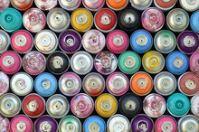 Large Number Of Used Colorful Spray Cans Of Aerosol Paint Lying On The Treated Wooden Surface In The Artist's Graffiti Workshop Close Up. Dirty And Stained Cans For Art