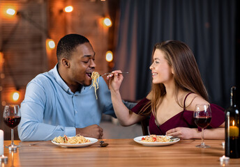 Wall Mural - Loving Interracial Couple Feeding Each Other With Spaghetti During Dinner In Restaurant