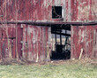 An old red barn, with peeling red paint has its doors open revealing items inside