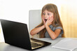 © Evgeniya Sheydt - A European girl uses a laptop to watch exciting videos. The girl looks surprised with her mouth open, hands at her mouth. Something shocked the girl. Big interest.