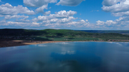 Poster - Aerial view of a reflecting river with mountain forests and buildings under the cloudy sky