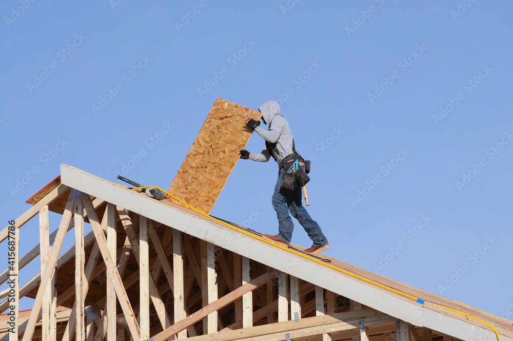 Construction worker installs plywood sheathing on a pitched roof frame ...