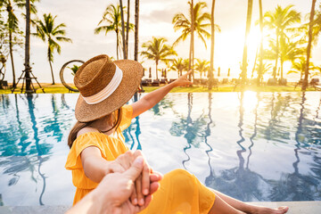 Young couple traveler relaxing and enjoying the sunset by a tropical resort pool while traveling for summer vacation