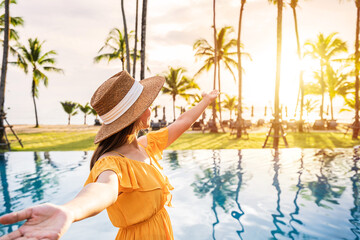 Young woman traveler relaxing and enjoying the sunset by a tropical resort pool while traveling for summer vacation