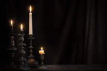 Antique Candlestick With Burning Candle On Old Wooden Table On Background Black Velvet Curtain