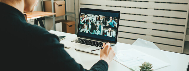 Wall Mural - Woman has video call with her teammates using laptop.  White loft workspace