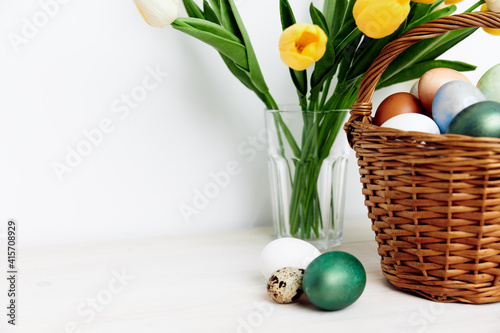 Obraz Dibond Easter eggs in a basket and yellow tulips in a vase In a bright room