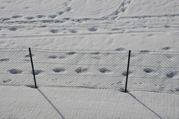 Wire fence with barbed wire. On a snowy meadow is a fence with metal posts and wire mesh. view from above. protective fence of prisons, waterworks, sources of drinking water. Overcoming is difficult