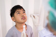 © arcyto - Doctor taking a swab for corona virus sample from potentially infected  boy nose. Covid-19 laboratory test.Medical staff with PPE suit test coronavirus covid-19 to asian kid by nose swab at hospital.