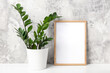 © IRINA - Wooden vertical frame with white blank card, and green houseplant flower in pot on table on gray concrete wall background. Mockup Template for your design, text