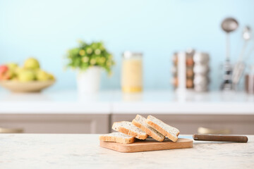 Board with toasts and knife on table in modern kitchen