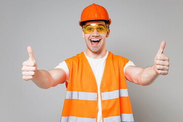 Wall Mural - Young employee happy handyman man in orange vest protective hardhat show thumbs up gesture isolated on grey background studio portrait. Instruments for renovation apartment room. Repair home concept.