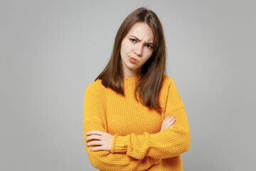 Young sad unhappy thoughtful pensive overthinking beautiful woman 20s wearing casual knitted yellow sweater hold hands crossed folded looking camera isolated on grey color background studio portrait.