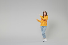 Full Length Of Young Smiling Positive Caucasian Happy Woman 20s In Knitted Yellow Sweater Stand Point Index Finger Aside On Workspace Copy Space Area Isolated On Grey Color Background Studio Portrait